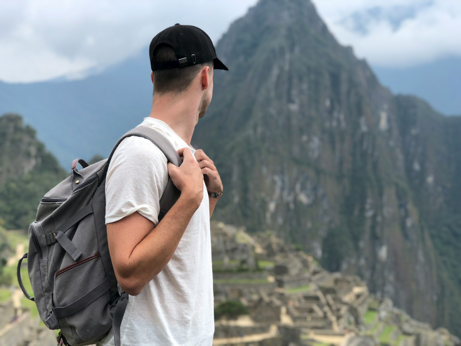 man wearing white shirt with backpack facing green mountain